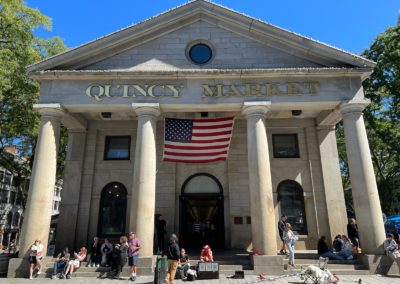 Group of tourists sitting at the entrance of the Quincy Market - a destination included in the Best of Boston Tour.