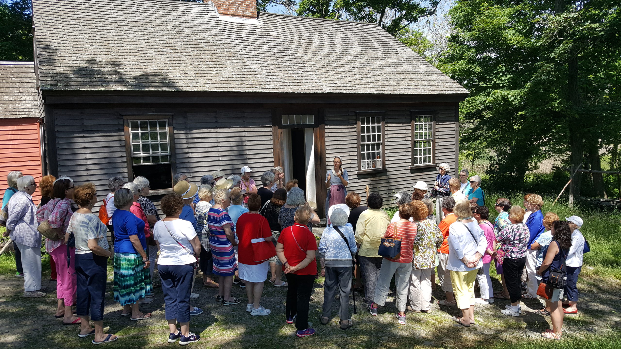 Group of tourists gathering at a cabin in Coggeshall Farm Museum - an experience included in the Life by the Bay Tour.